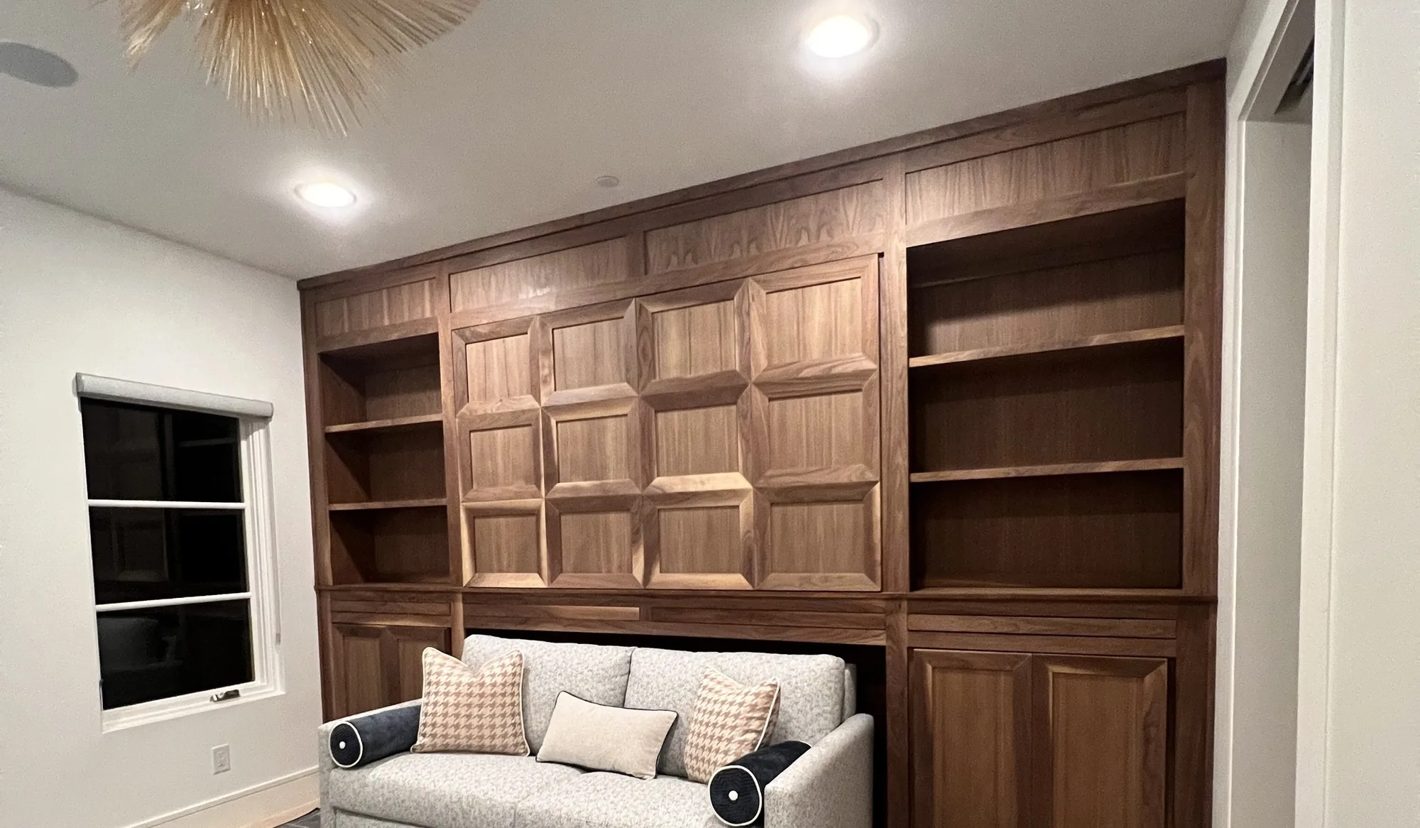 A floor-to-ceiling built-in wall in stained wood with open shelving and panelled center doors