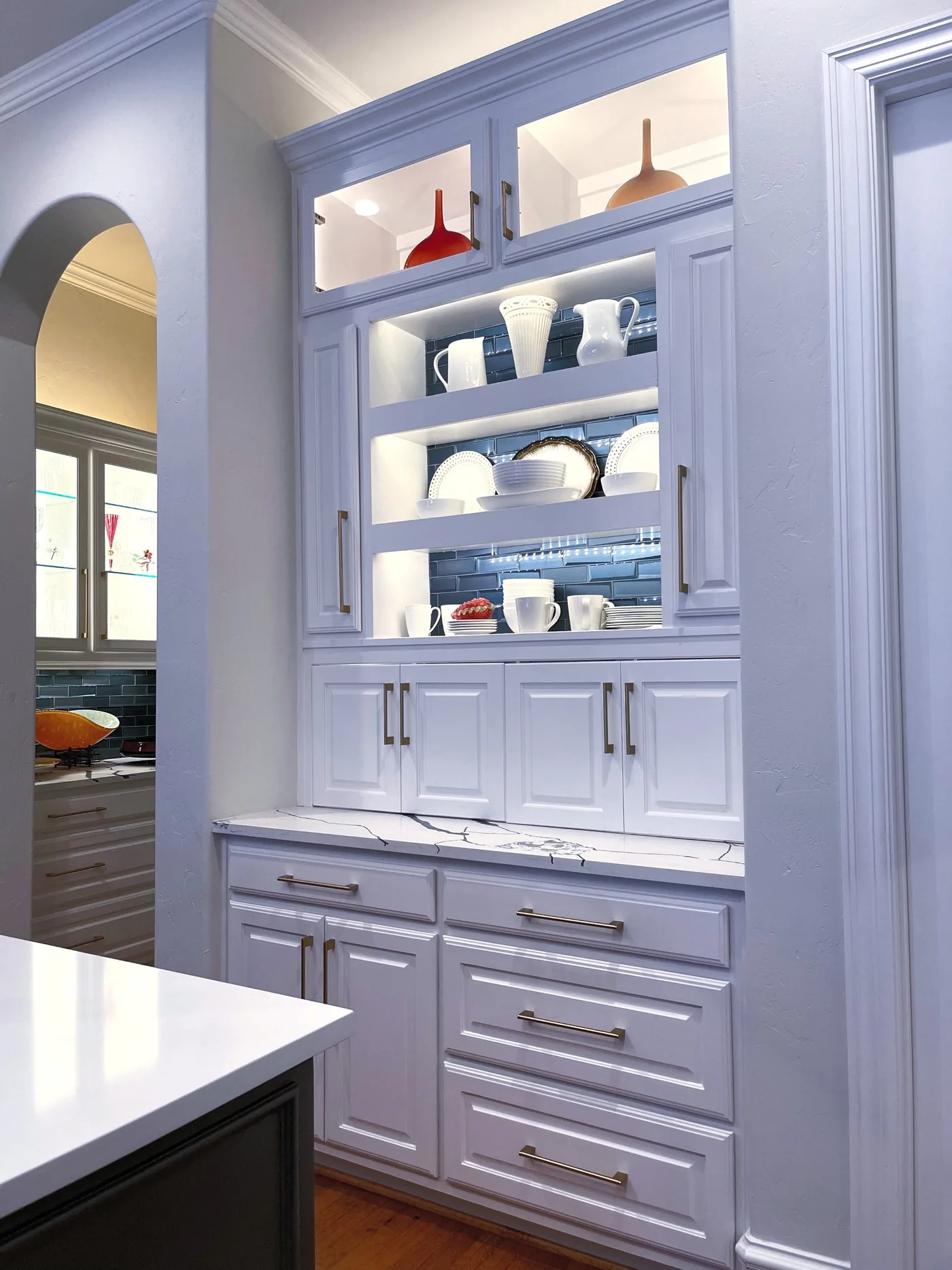 Glass-front upper cabinets lit from inside above a run of painted base cabinets