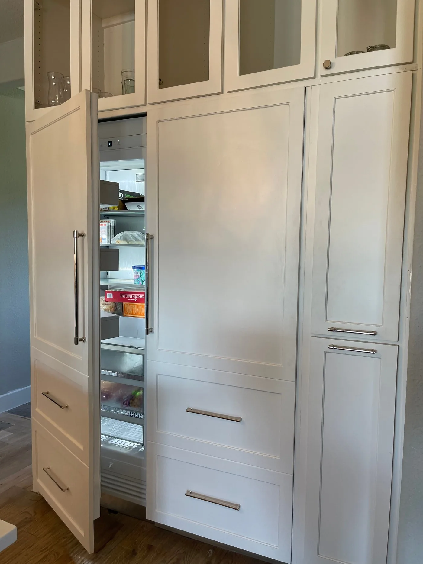 Full-height pull-out pantry standing open beside panel-front cabinet doors