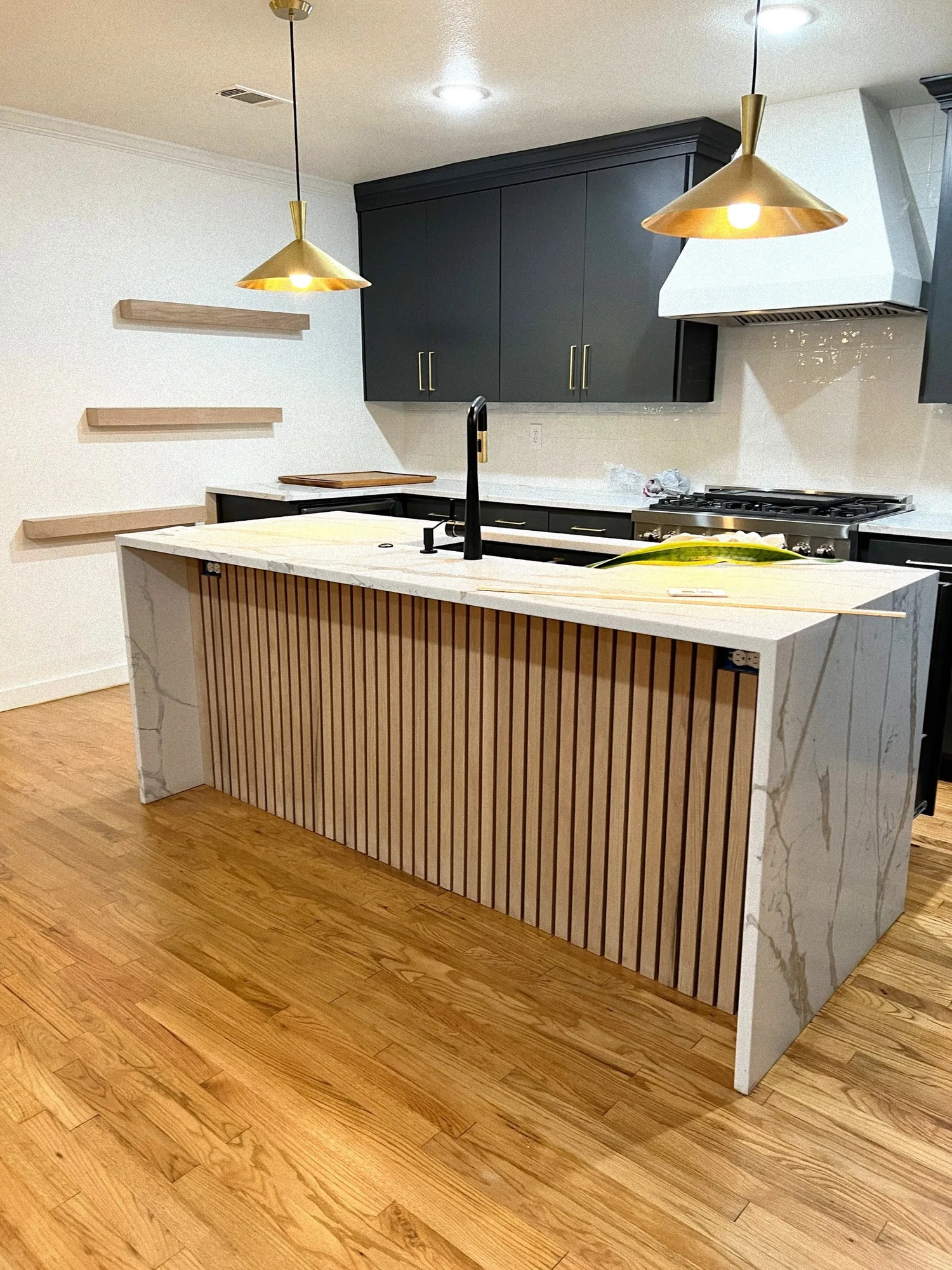 Kitchen island with a slatted wood face and a stone waterfall edge, under brass pendants