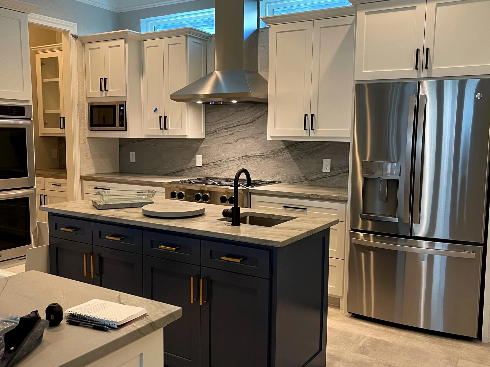 Kitchen with a deep navy island, brass pulls, cream perimeter cabinets, and a stone backsplash